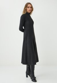 Abito grigio a maniche lunghe con collo alto, silhouette fluida e morbida al tatto. Abbinato a stivali neri con tacco al ginocchio.