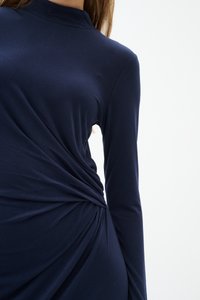 Marinblå långärmad klänning i mjukt tyg, med en vriden design vid midjan som skapar en draperad struktur och form.