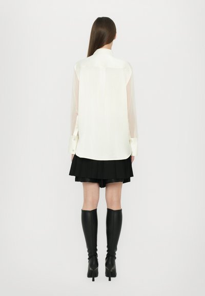 White shirt with sheer sleeves, pleated black skirt, and knee-high black boots. Smooth fabric with button details on the cuffs.