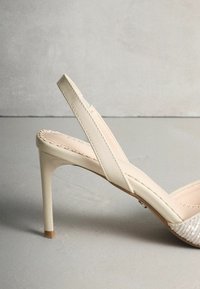Beige slingback hak met een hoge naaldhak, gladde leren bandjes en een glinsterend zilveren sequined teengebied. Ronde tenen vorm.