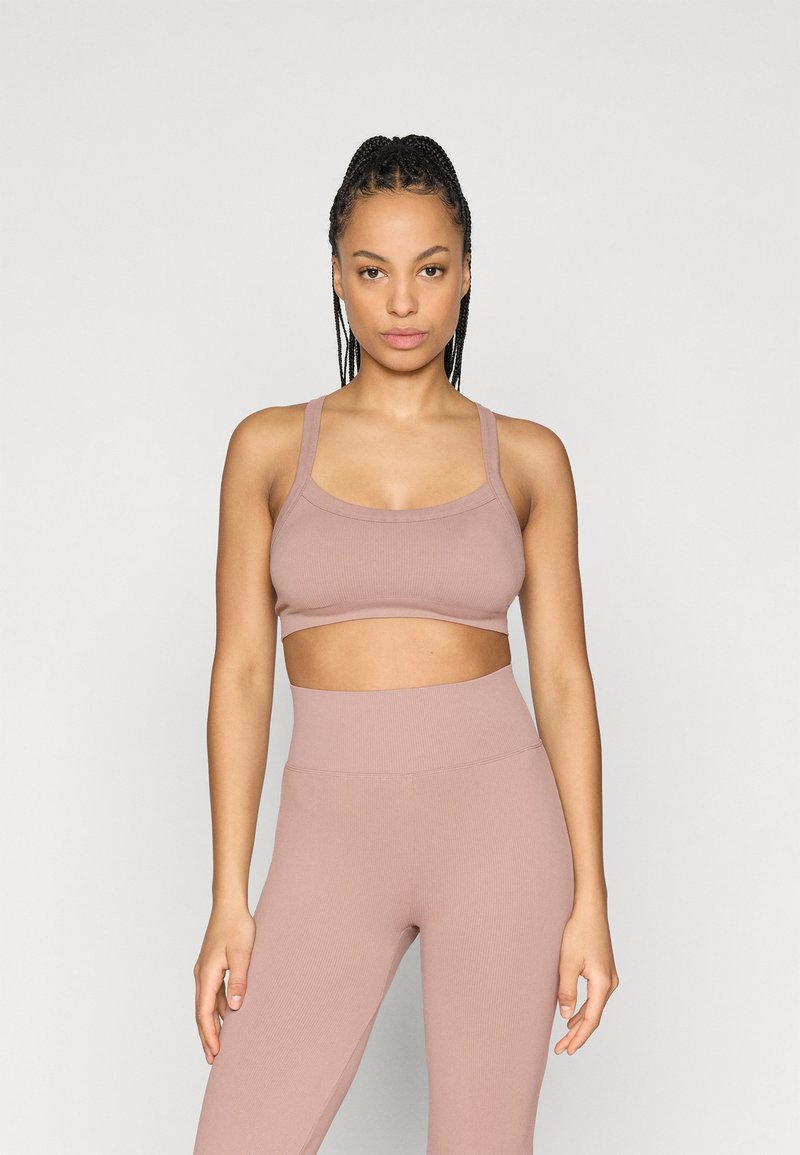 Lichtroze geribbelde sportbeha met brede bandjes, een lage ronde hals en bijpassende high-waisted leggings met een gladde textuur.