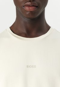 Light beige short-sleeve t-shirt made of soft fabric. Features a subtle embossed "BOSS" logo on the chest. Round neckline.