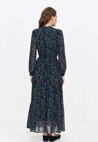 Navy floral maxi dress with long sleeves, cinched waist, tiered skirt, and sheer fabric featuring green and white flower patterns.