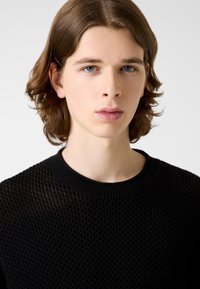 Schwarzer Strickpullover mit strukturiertem Muster und rundem Ausschnitt, mit lockerem Sitz und leichter Transparenz im Stoff.