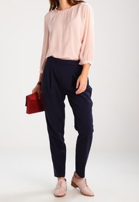 Ljusrosa blus med samlad hals, marinblå tapered byxor med elastisk midja, rosa snörskor och en röd clutchväska.