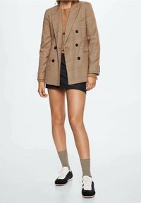 Brązowa, kratowana marynarka dwurzędowa na beżowej bluzce, zestawiona z czarną mini spódniczką. Dopełniona szarymi skarpetkami i czarnymi trampkami.