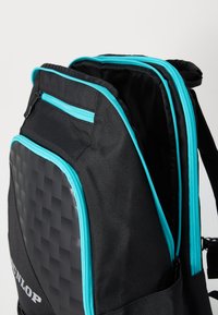 Schwarzer Rucksack mit türkisfarbenen Reißverschlüssen, ausgestattet mit einer strukturierten, glänzenden schwarzen Fläche und mehreren Fächern. Hochdichtes Material für Langlebigkeit.