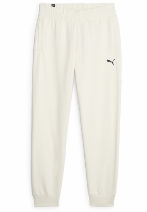 Pantaloni della tuta color crema realizzati in un tessuto morbido, con cintura elastica, tasche laterali e un piccolo logo nero sulla coscia sinistra.