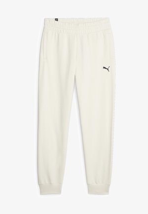 Pantaloni della tuta color crema realizzati in un tessuto morbido, con cintura elastica, tasche laterali e un piccolo logo nero sulla coscia sinistra.