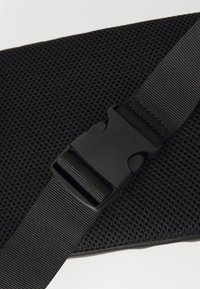 Tessuto a rete nero con una superficie texturizzata, dotato di una fibbia in plastica nera e di una cinghia regolabile per una chiusura sicura.