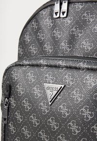 Zaino in finta pelle grigia con motivo a logo ripetuto, logo metallico triangolare e doppia zip con tiranti.