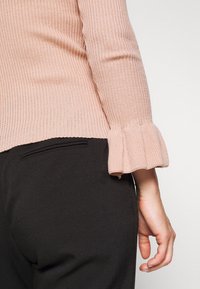 Helles rosa Rippstrickoberteil mit Rüschensäumen, kombiniert mit schwarzen, taillierten Hosen. Glatte Textur mit tailliertem Schnitt.