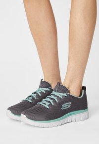 Sneakers athletic grigi con tomaia in rete, lacci turchesi e suola bianca. Presentano un logo sul lato e una superficie testurizzata per una migliore aderenza.