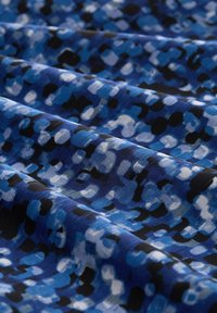 Ein Stoff mit einem blauen und schwarzen Muster aus unregelmäßigen Formen. Der Stoff hat eine glatte Textur und zeigt eine Mischung aus hellen und dunklen Farbtönen.