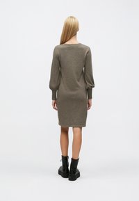 Dzianinowa sukienka z długim rękawem w oliwkowej zieleni o luźnym fasonie, z prążkowanymi mankietami i zaokrąglonym dekoltem, zestawiona z czarnymi masywnymi botkami za kostkę.