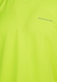 Neon keltainen urheilupaita, joka on valmistettu kevyestä, teksturoidusta kankaalta; siinä on V-pääntie ja sana "KESTÄVYYS" painettuna harmaana.