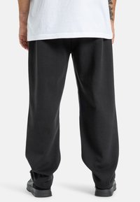 Czarne dresy wykonane z miękkiego materiału, z luźnym krojem i elastycznymi mankietami. Noszone z białą koszulką, o prostym wzorze.