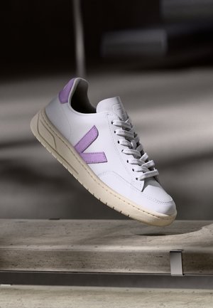 Baskets en cuir blanc avec des accents violet clair, une semelle beige texturée et des lacets plats au design minimaliste, ornées d'un logo en relief.