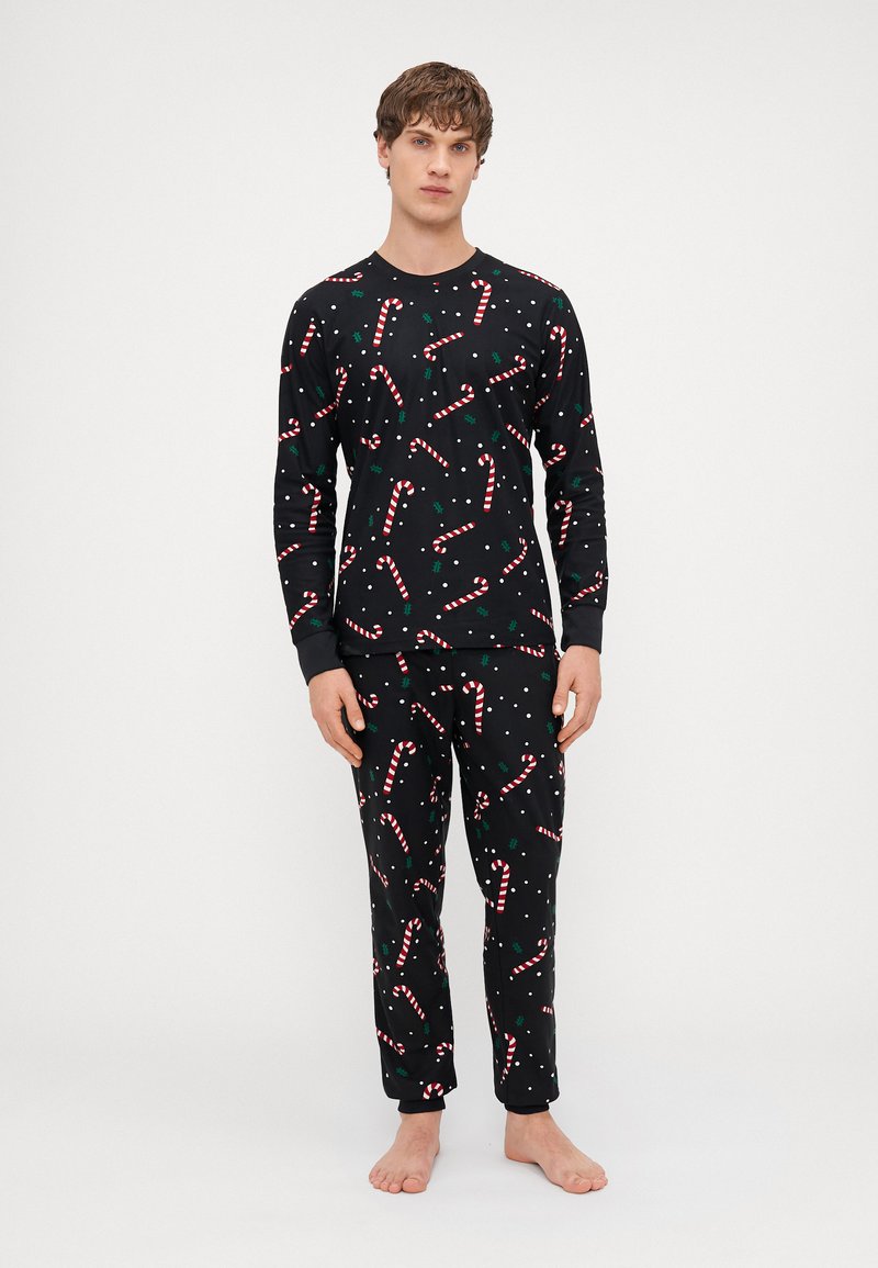Schwarzes Schlafanzug-Set mit einem Zuckerstangen- und Stechpalmenmuster, hergestellt aus einem weichen Stoff mit langen Ärmeln und elastischen Bündchen an den Hosen.