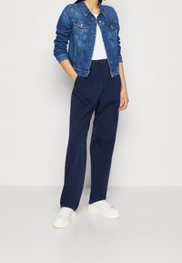 Džínová bunda s klasickým střihem, světle modré barvy, s náprsními kapsami, kombinovaná s širokými kalhotami námořnické modři a bílými teniskami.