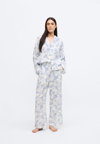 Ensemble de pyjama léger à manches longues, avec des motifs floraux bleus sur fond blanc ; tissu doux et ample, silhouette décontractée.