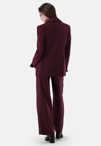 Completo bordeaux caratterizzato da un blazer sartoriale con colletto a incisione e pantaloni a gamba larga, realizzato in un tessuto liscio.