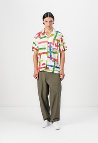 Short-sleeved shirt with a white base, featuring colorful graphic patterns in red, green, and blue. Paired with loose olive-green pants.