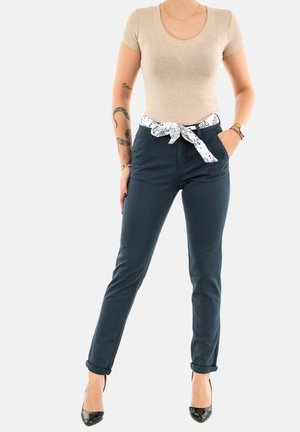 Navy trousers with rolled cuffs, featuring a white patterned belt. Paired with a beige fitted t-shirt. Smooth fabric with a tailored fit.