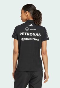 Černé polo tričko s límečkem, na zadní straně s bílými sponzorskými logy včetně "PETRONAS" a "CROWDSTRIKE". Krátké rukávy zdobené akcenty.