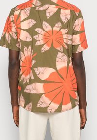 Kortærmet skjorte i grønne stoffer, med store orange og pink blomster mønstre. Runde kant med synlige syninger.
