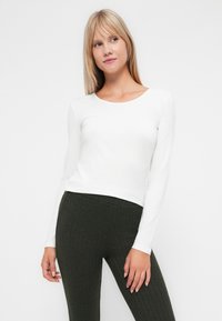 Witte lange mouw top met een ronde halslijn. Gecombineerd met olijfgroene geribde leggings, met een zachte textuur en een aansluitend ontwerp.