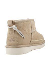Stivaletto in suede beige con fodera in shearling bianco, linguetta posteriore e dettagli di cucitura bianchi, posato su una suola bianca testurizzata.