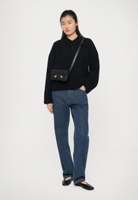 Maglione nero lavorato a maglia con scollo a V, motivo testurizzato, abbinato a jeans blu a gamba dritta e ballerine nere; piccola borsa a tracolla nera.