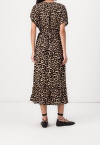 Robe midi imprimée léopard avec des manches courtes, ourlet volé, détail croisé à la taille, et portée avec des chaussures plates noires. Texture de tissu lisse.