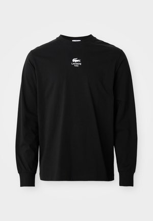 Must mustahem T-särk, pikkade varrukatega, valmistatud puuvillast, klassikalise ümmarguse kaelusega ning rinnal on tikitud valge Lacoste logo. Lihtne ja klassikaline disain.
