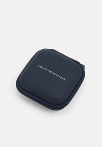 Tamsiai mėlyna užtrauktuku užsegama dėžutė su lygiu paviršiumi, su "TOMMY HILFIGER" logotipu baltos spalvos, stačiakampio formos, tinkama aksesuarams ar laikymui.