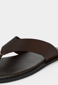 Σανδάλι από σκούρο καφέ δέρμα με φαρδιά λουρίδα, μαύρη σόλα και επενδεδυμένο εσωτερικό πέλμα, σχεδιασμένο για καθημερινή χρήση.