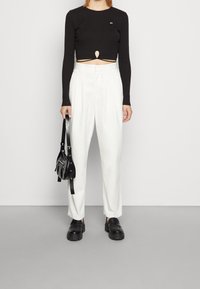 Svart ribbat långärmad crop top med nyckelhål; vita plisserade höga byxor; svarta klumpiga skor; liten svart väska.