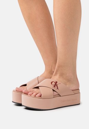 Sandales à plateforme rose clair avec un design à lanières croisées, fabriquées en matériau synthétique, dotées d'un logo et d'une semelle texturée pour une meilleure adhérence.