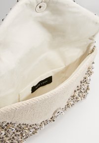 Beige tygclutch med silverfärgade pärldekorationer, magnetisk snäppstängning och en slät innerfoder. Etikett: "NEW LOOK."