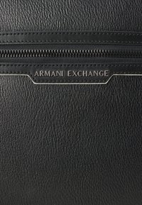 Borsa nera in pelle con zip, dalla superficie texture, dotata di un logo "Armani Exchange" in tono argento e cuciture pulite lungo la cerniera.