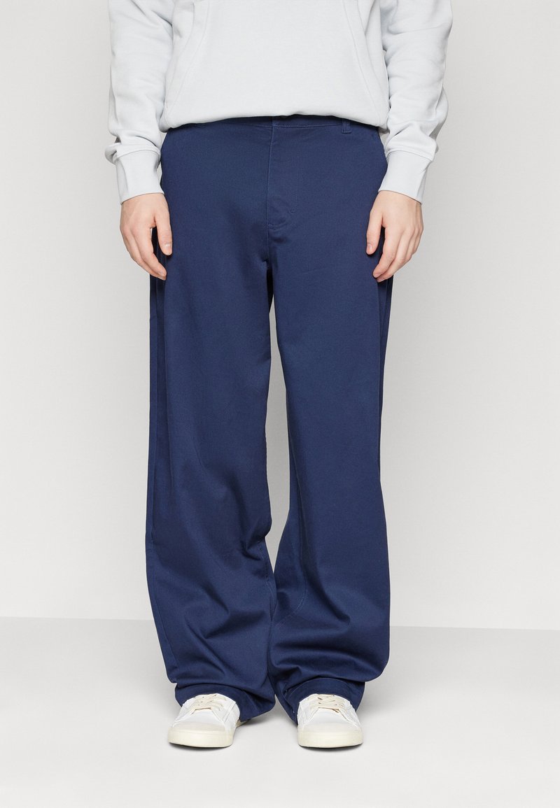 Pantaloni a gamba larga blu navy in tessuto morbido, con vita elastica. Abbinati a scarpe di colore chiaro per un look casual.