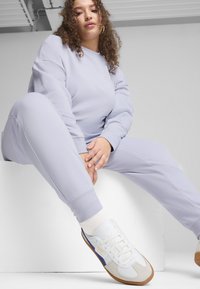 Svetlo vijolična trenirka in usklajeni hlače iz mehkega materiala. Bele športne copate z modrimi in peščenimi detajli. Priložnostna, sproščena prova.