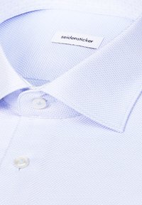 Chemise habillée bleu clair texturée avec un col boutonné et une étiquette blanche portant la mention "seidensticker" à l’intérieur du col.
