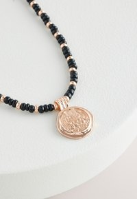 Black beaded necklace with rose gold accents and a circular pendant featuring intricate engraving and textural details.