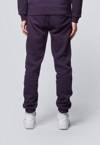 Dark purple sweatpants made of soft fabric, featuring elastic cuffs, a relaxed fit, and paired with white sneakers.