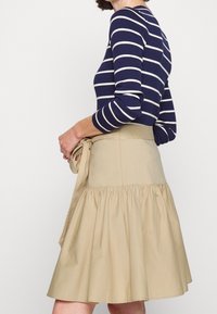 Marine gestreifter Pullover mit taillierter Passform und gerippter Textur. Beigefarbener, knielanger, ausgestellter Rock mit gerafftem Saum und seitlichem Bindeband.