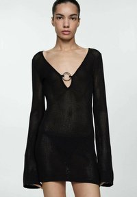 Rochie tricotată neagră cu decolteu adânc în V și mâneci lungi, având un accent circular metallic la linia gâtului.