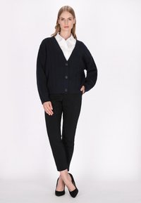 Marine gebreide cardigan met een V-hals, drie grote knopen en geribbelde manchetten, gecombineerd met zwarte slim-fit broeken en zwarte hakken.
