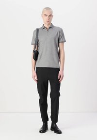 Pelēks polo krekls ar pus-izmēra rāvējslēdzēja apkakli, apvienots ar melnām formas biksēm un melnām potīšu zābakiem; modelis arī nes mazu melnu somu.